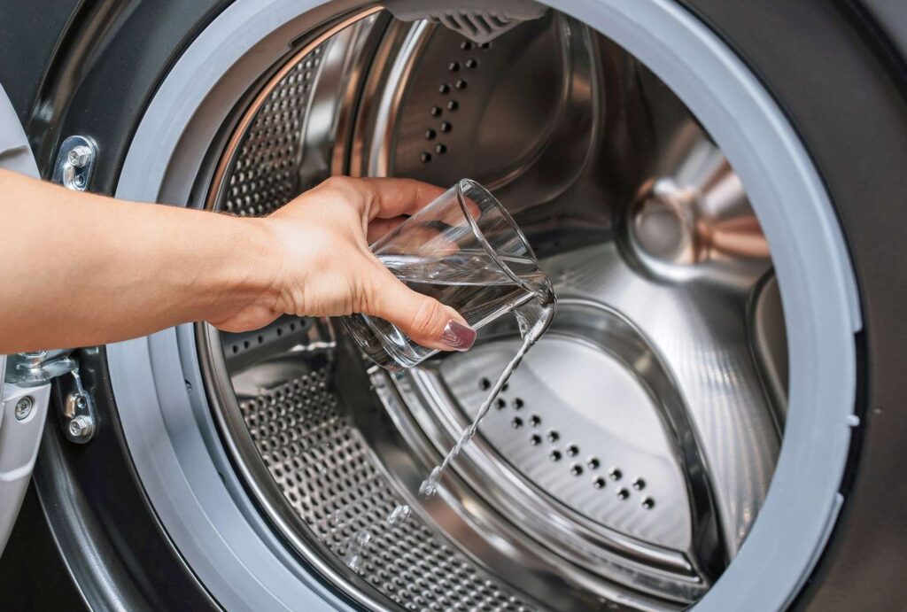Woman placing a bottle of vinegar on the washing machine, a natural and effective solution for maintaining freshness and cleanliness in laundry appliances