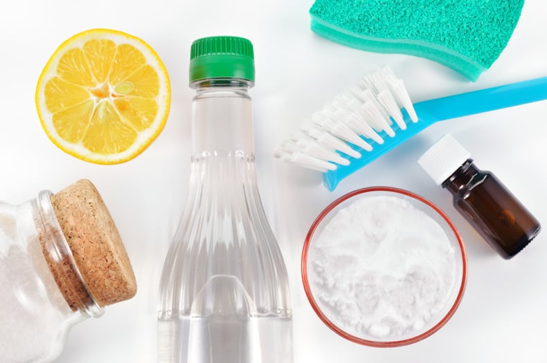 Assorted cleaning supplies laid out, including vinegar, baking soda, microfiber cloth, and a scrub brush, ready for use in cleaning a washing machine